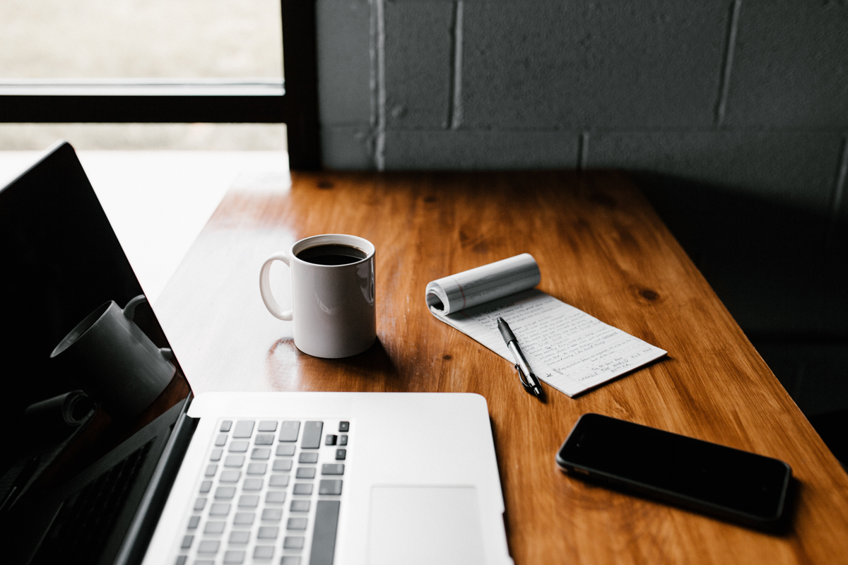 MacBook Pro, white ceramic mug, and black smartphone on table - Credit to @andrewtneel, image supplied via Unsplash